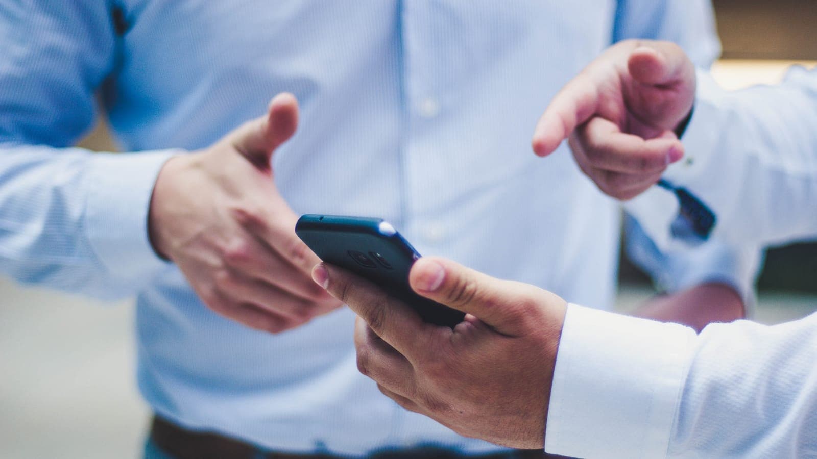 Deux professionnels en chemise échangent autour d'un téléphone, l'un pointant l'écran