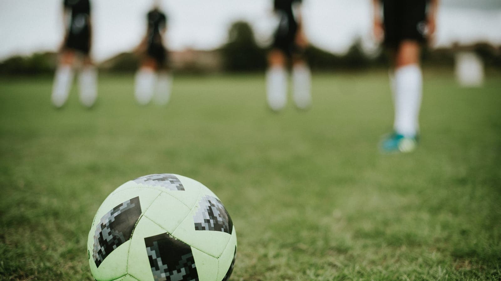 Jambes de jeunes joueurs alignés sur une pelouse, un ballon au premier plan