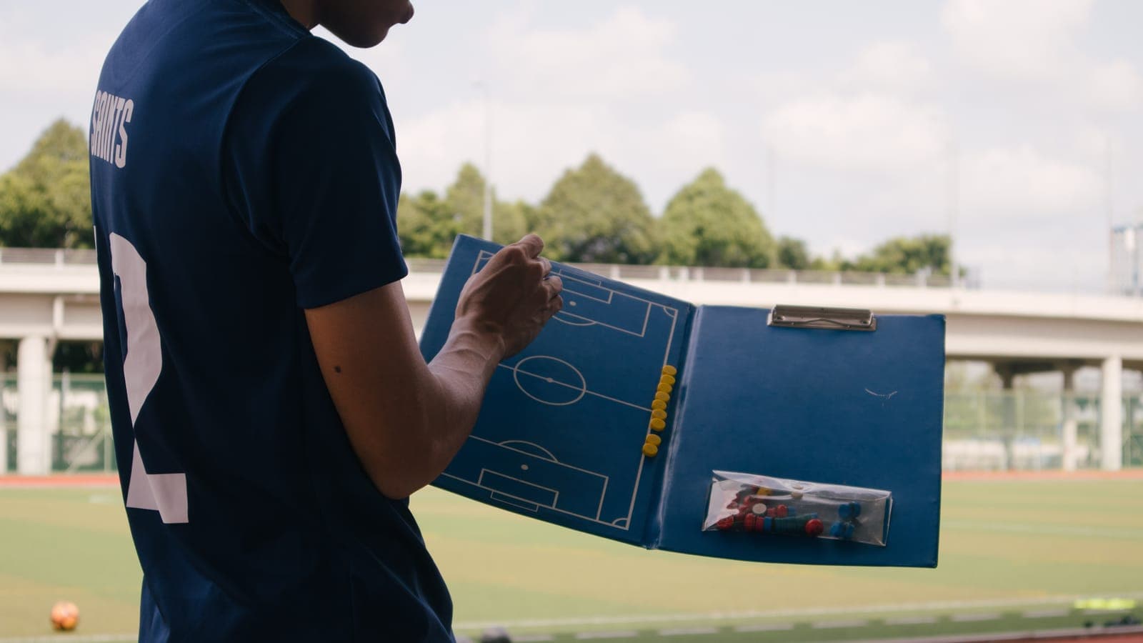 Un joueur en maillot bleu consulte un tableau tactique au bord d'un terrain