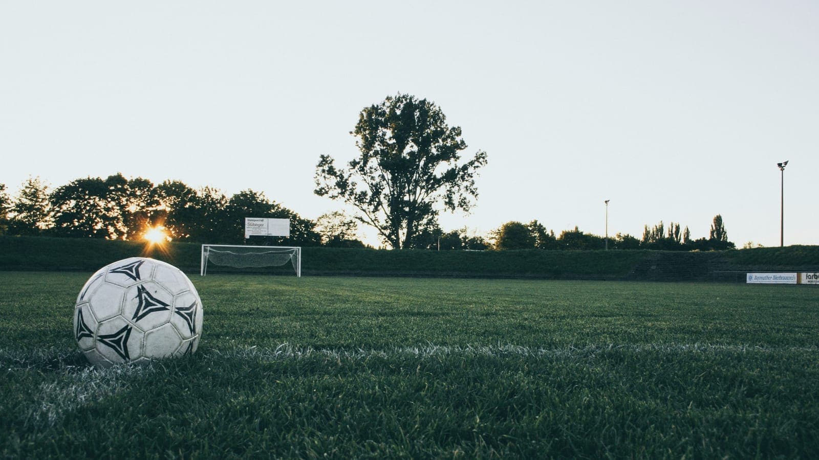 Un ballon de football posé sur une pelouse au crépuscule, cage de but en arrière-plan